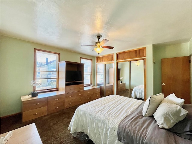 bedroom featuring two closets, a ceiling fan, and dark colored carpet