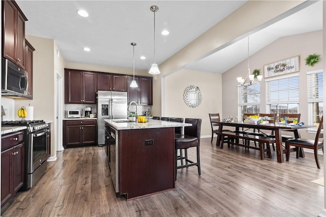 kitchen featuring dark wood-type flooring, a breakfast bar, an island with sink, decorative light fixtures, and appliances with stainless steel finishes