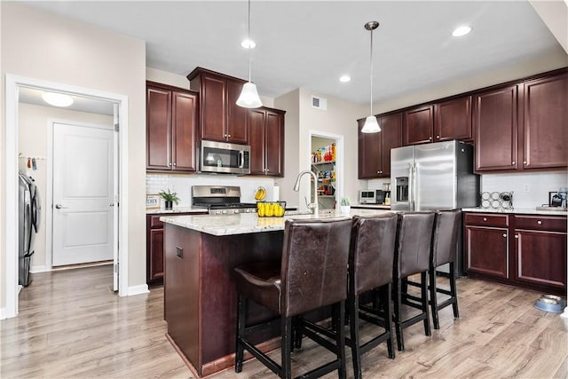 kitchen featuring visible vents, light wood-style flooring, a kitchen breakfast bar, tasteful backsplash, and stainless steel appliances