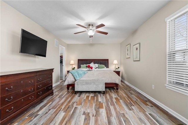 bedroom with ceiling fan, visible vents, baseboards, and wood finished floors