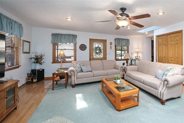 living area featuring light wood-style flooring, a skylight, and a ceiling fan