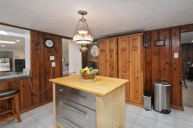 kitchen with wooden walls, light floors, butcher block counters, hanging light fixtures, and a textured ceiling