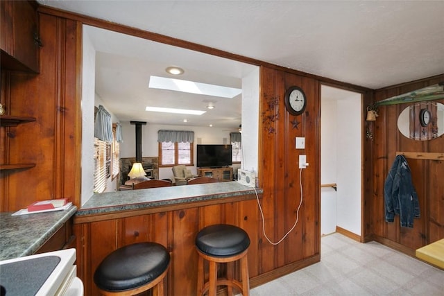 kitchen featuring a breakfast bar area, brown cabinetry, a skylight, light floors, and a wood stove