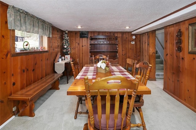 dining room with stairway, light colored carpet, wood walls, and a textured ceiling