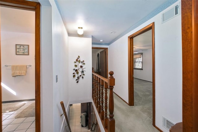 hall featuring baseboards, an upstairs landing, visible vents, and light carpet