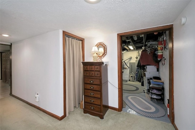 hall featuring baseboards, light carpet, and a textured ceiling