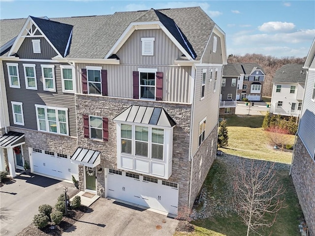 view of front of house with board and batten siding, a shingled roof, driveway, stone siding, and an attached garage