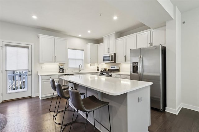 kitchen featuring dark wood-style floors, a sink, stainless steel appliances, white cabinets, and a center island