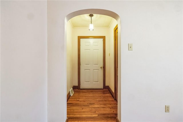 corridor with visible vents, baseboards, ornamental molding, wood finished floors, and arched walkways