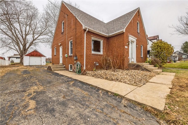 view of front of property with brick siding, a shingled roof, a detached garage, aphalt driveway, and an outbuilding