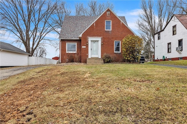 view of front of house with a front yard, cooling unit, fence, a shingled roof, and brick siding