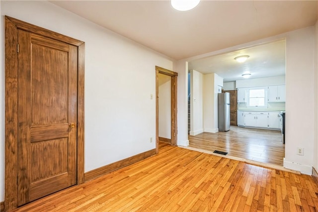 empty room with light wood-style floors, visible vents, and baseboards