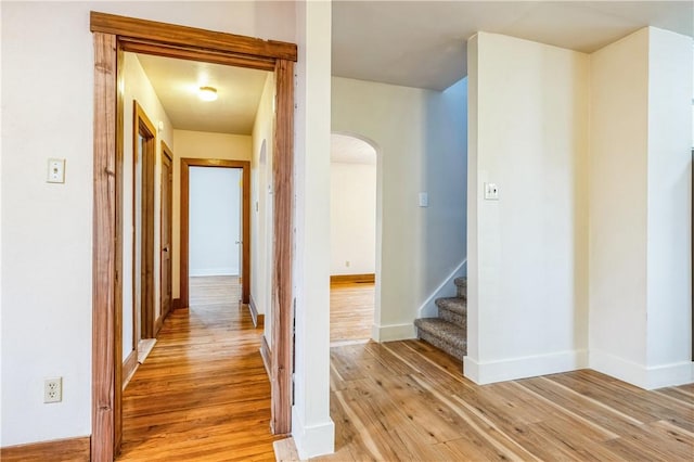 hallway with light wood-type flooring, arched walkways, baseboards, and stairs