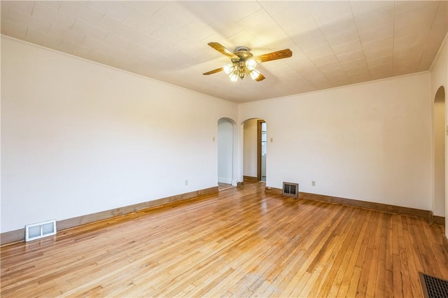 empty room featuring visible vents, arched walkways, a ceiling fan, and light wood finished floors