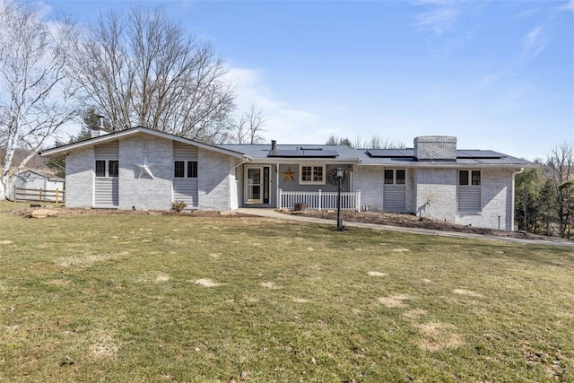 view of front of home featuring roof mounted solar panels, covered porch, a front yard, brick siding, and a chimney