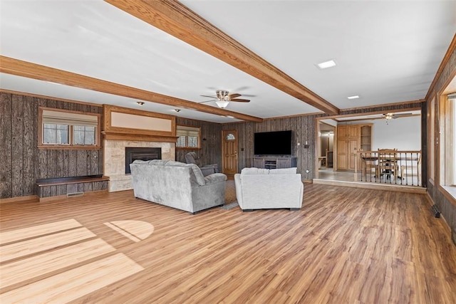 unfurnished living room featuring wood finished floors, beam ceiling, a fireplace with raised hearth, and ceiling fan