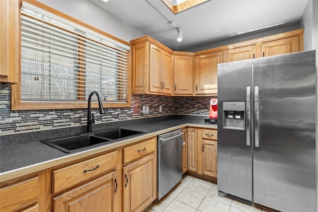 kitchen with light tile patterned flooring, a sink, appliances with stainless steel finishes, dark countertops, and backsplash