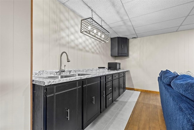 kitchen featuring dark cabinetry, light wood-style flooring, a drop ceiling, a sink, and light countertops