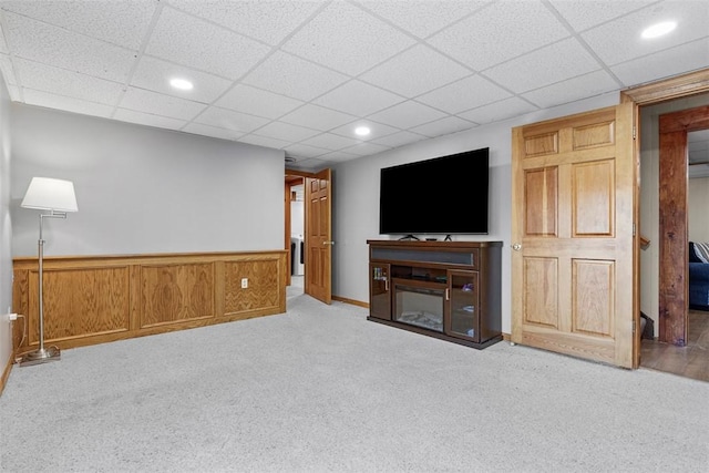 living room featuring a wainscoted wall, a drop ceiling, carpet flooring, recessed lighting, and a glass covered fireplace