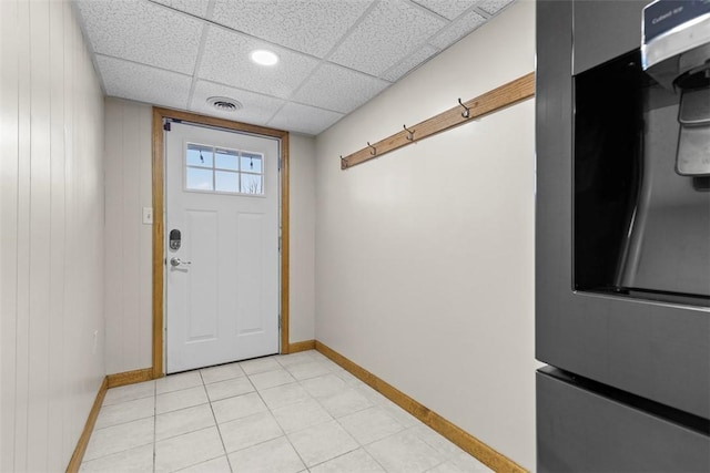 foyer entrance featuring visible vents, wooden walls, baseboards, light tile patterned floors, and a paneled ceiling