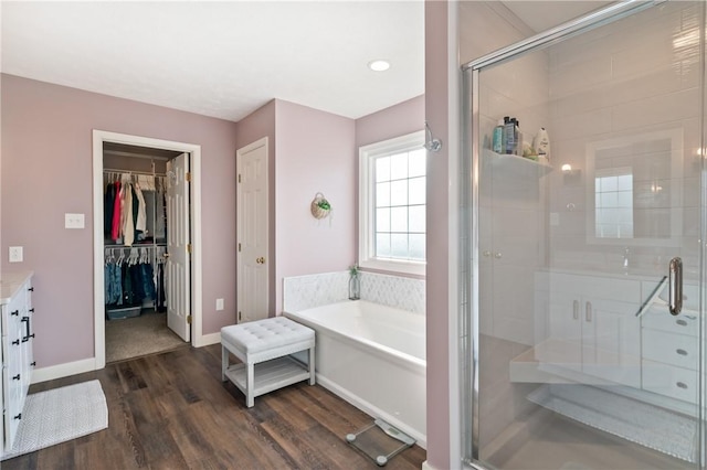 full bathroom featuring a garden tub, a stall shower, wood finished floors, baseboards, and a spacious closet