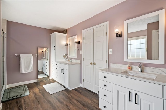 full bath with a sink, baseboards, two vanities, and wood finished floors