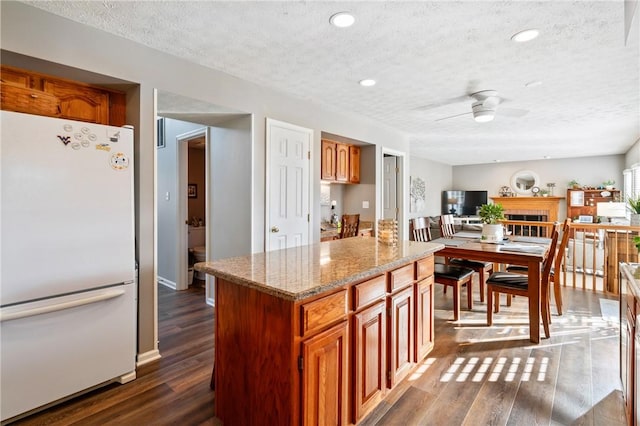 kitchen featuring light stone countertops, dark wood-style flooring, freestanding refrigerator, ceiling fan, and a textured ceiling