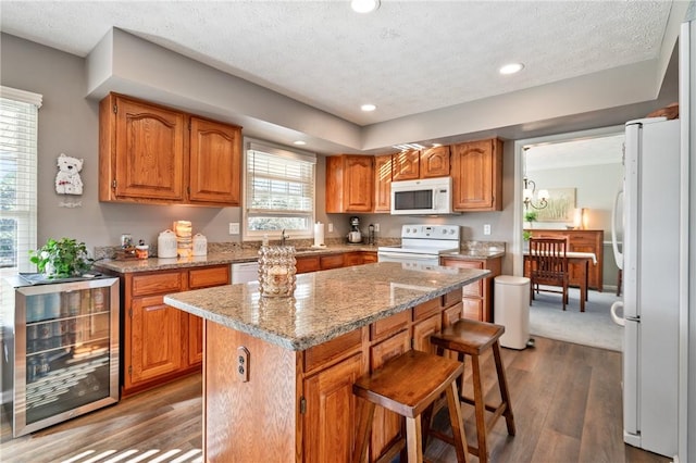 kitchen featuring a kitchen island, wine cooler, brown cabinets, white appliances, and dark wood-style flooring