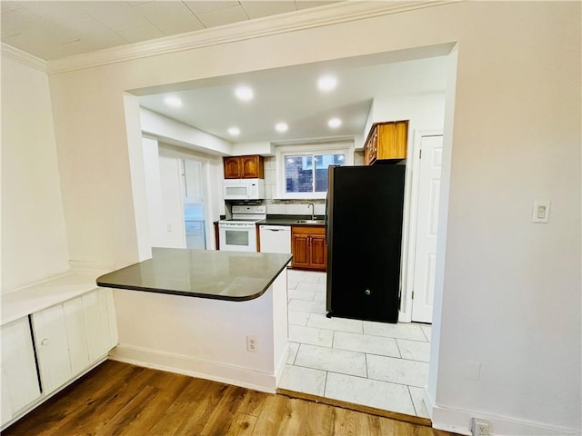 kitchen with dark countertops, ornamental molding, light wood-style flooring, white appliances, and a sink