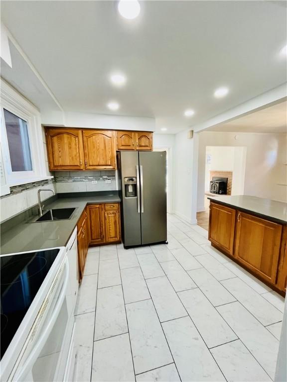 kitchen featuring white electric stove, stainless steel fridge with ice dispenser, a sink, dark countertops, and brown cabinets