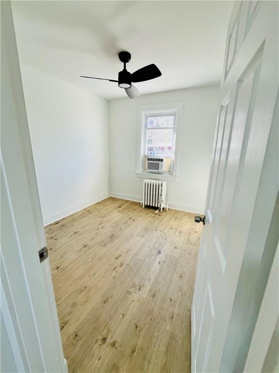 unfurnished bedroom with radiator, cooling unit, baseboards, ceiling fan, and light wood-style floors