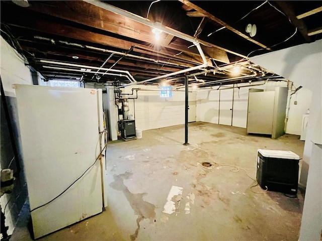 unfinished below grade area with washer / clothes dryer, a heating unit, and freestanding refrigerator