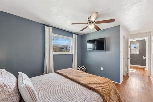 bedroom with baseboards, a textured ceiling, hardwood / wood-style floors, and a ceiling fan