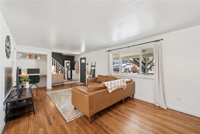 living area featuring stairs, built in shelves, wood finished floors, and baseboards