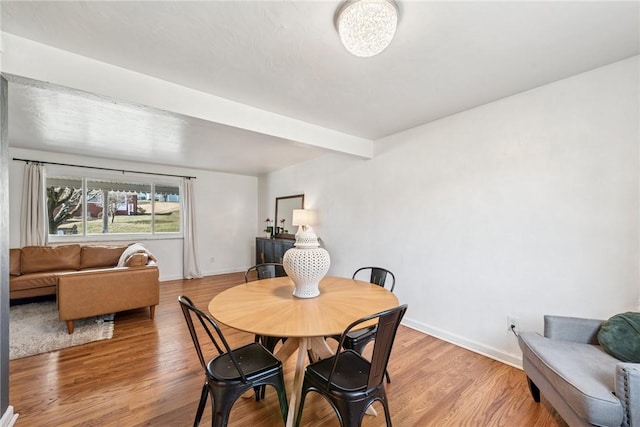 dining area featuring beamed ceiling, baseboards, and light wood finished floors