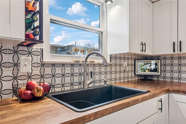 kitchen with butcher block countertops, backsplash, white cabinetry, and a sink