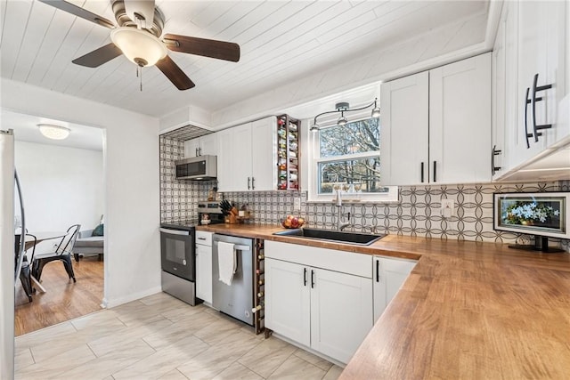 kitchen featuring a sink, stainless steel appliances, white cabinetry, backsplash, and butcher block counters