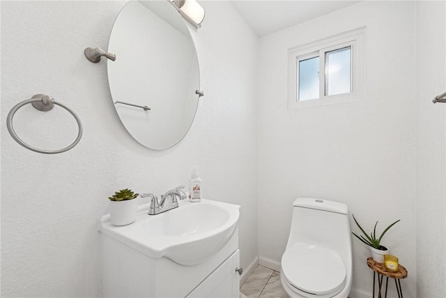 half bathroom featuring toilet, vanity, marble finish floor, and baseboards