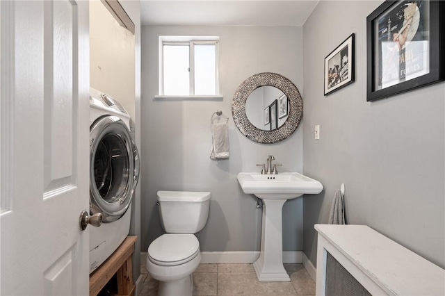 half bathroom with tile patterned flooring, washer / dryer, toilet, and baseboards