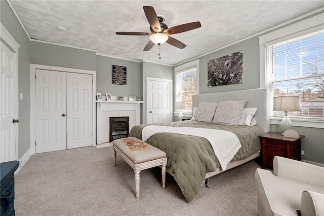 carpeted bedroom featuring two closets, baseboards, a fireplace with flush hearth, ornamental molding, and a ceiling fan