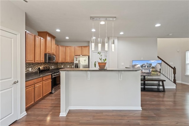 kitchen featuring a kitchen bar, dark wood-type flooring, backsplash, dark countertops, and stainless steel appliances