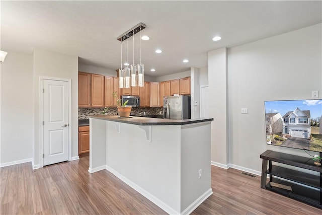 kitchen with wood finished floors, visible vents, appliances with stainless steel finishes, dark countertops, and backsplash