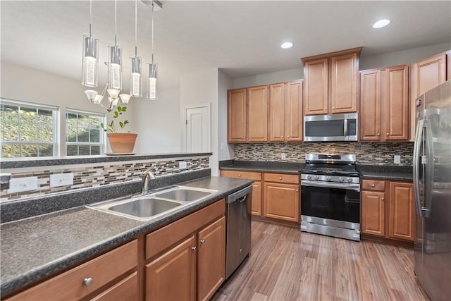 kitchen featuring dark countertops, light wood finished floors, an inviting chandelier, stainless steel appliances, and a sink