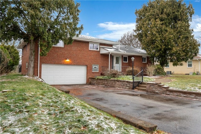 tri-level home with driveway, a front lawn, a garage, central air condition unit, and brick siding