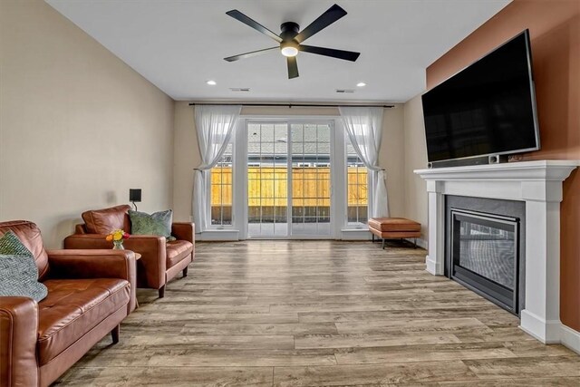 living room with a glass covered fireplace, recessed lighting, a ceiling fan, and wood finished floors