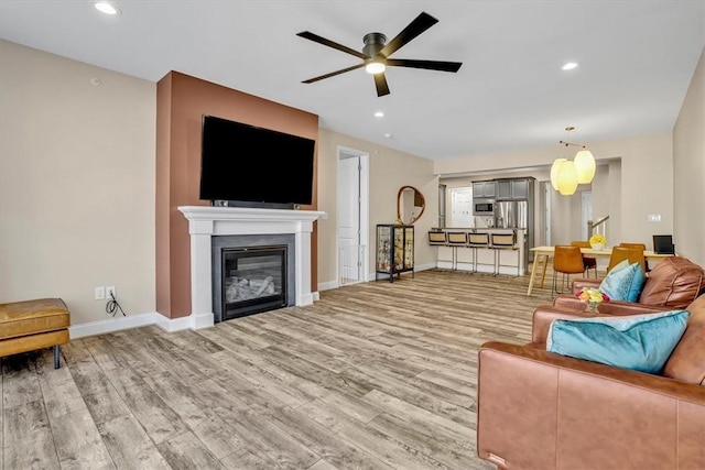 living area with a glass covered fireplace, recessed lighting, light wood-type flooring, and baseboards