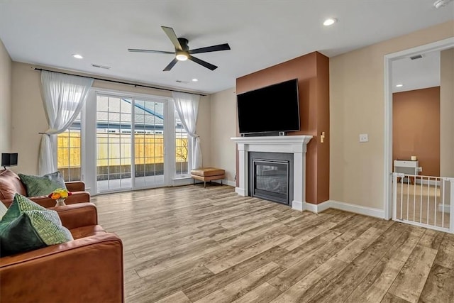 living room featuring a glass covered fireplace, recessed lighting, wood finished floors, and visible vents