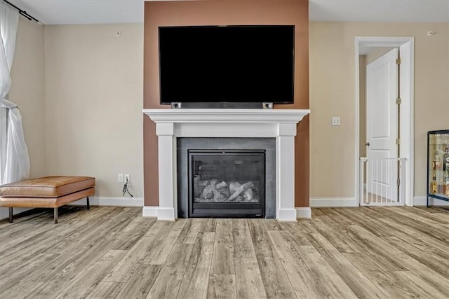 living room featuring a glass covered fireplace, baseboards, and wood finished floors