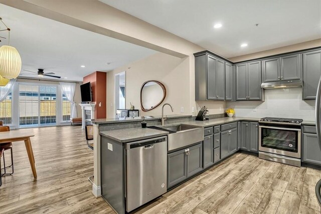 kitchen with gray cabinets, a sink, under cabinet range hood, appliances with stainless steel finishes, and open floor plan