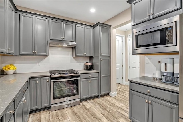 kitchen featuring under cabinet range hood, gray cabinets, stainless steel appliances, and light wood-style floors